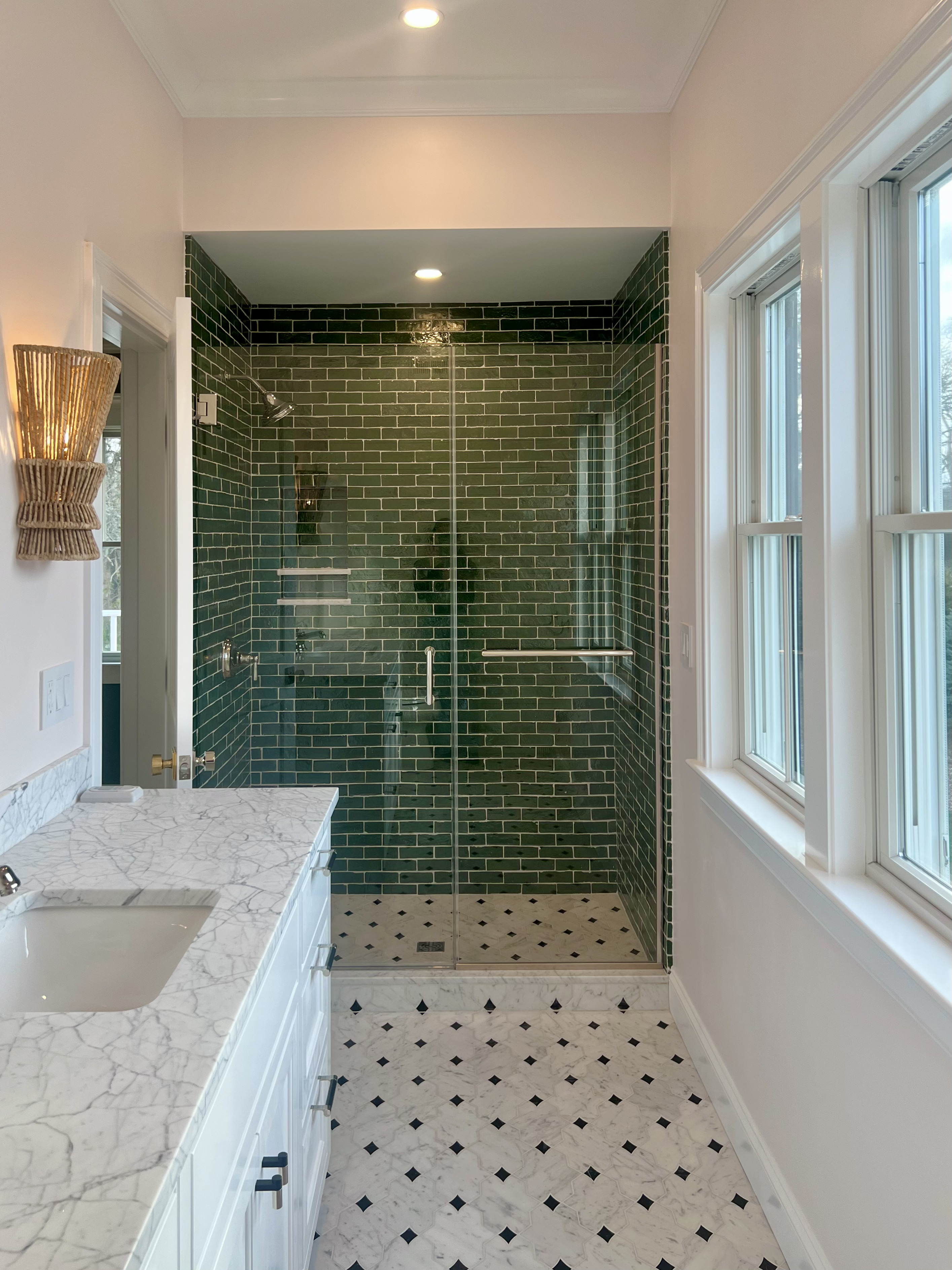 Green tiled shower with a glass enclosure, marble vanity and patterned floor