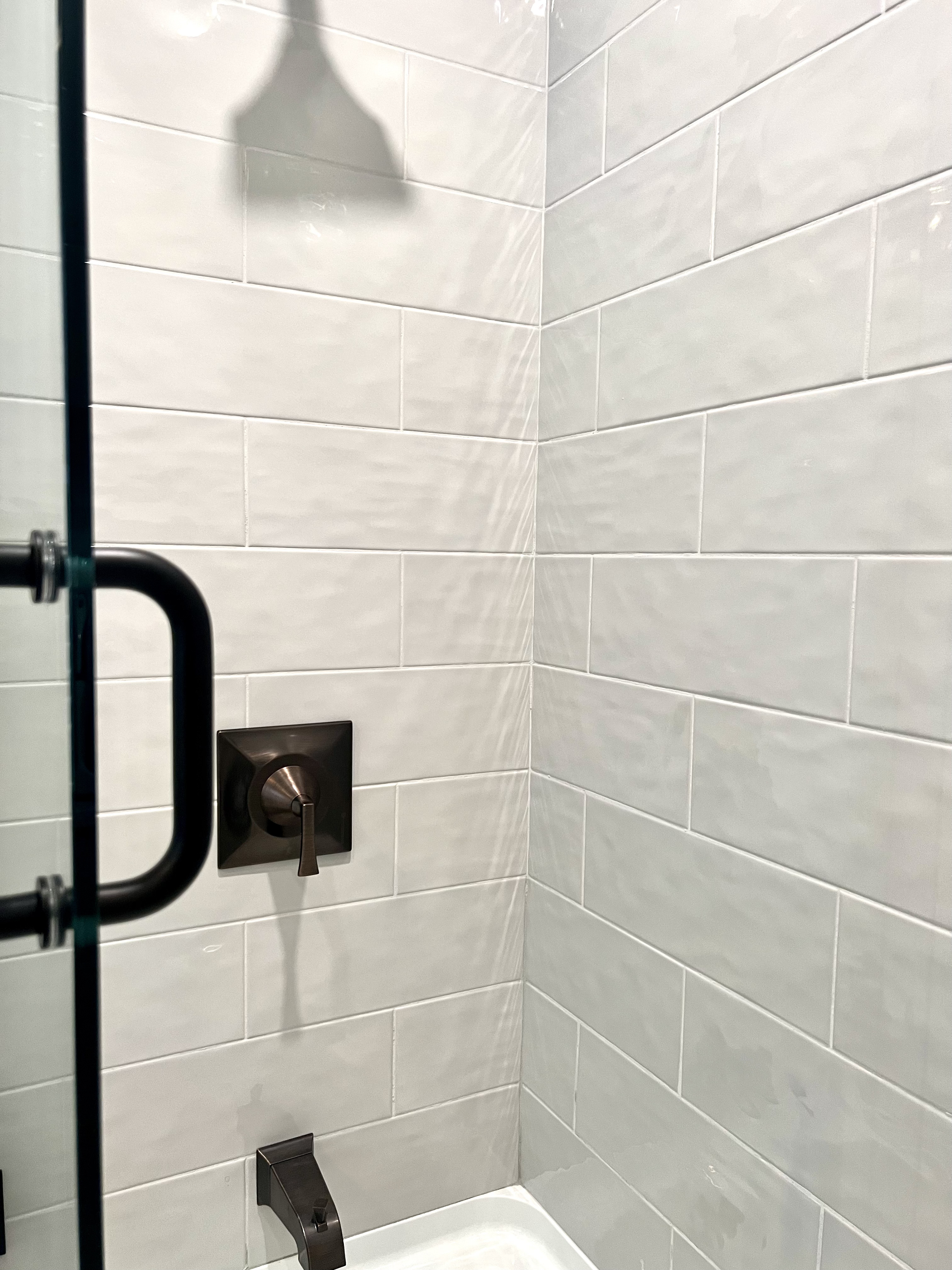 White tiled shower wall with bronze fixtures
