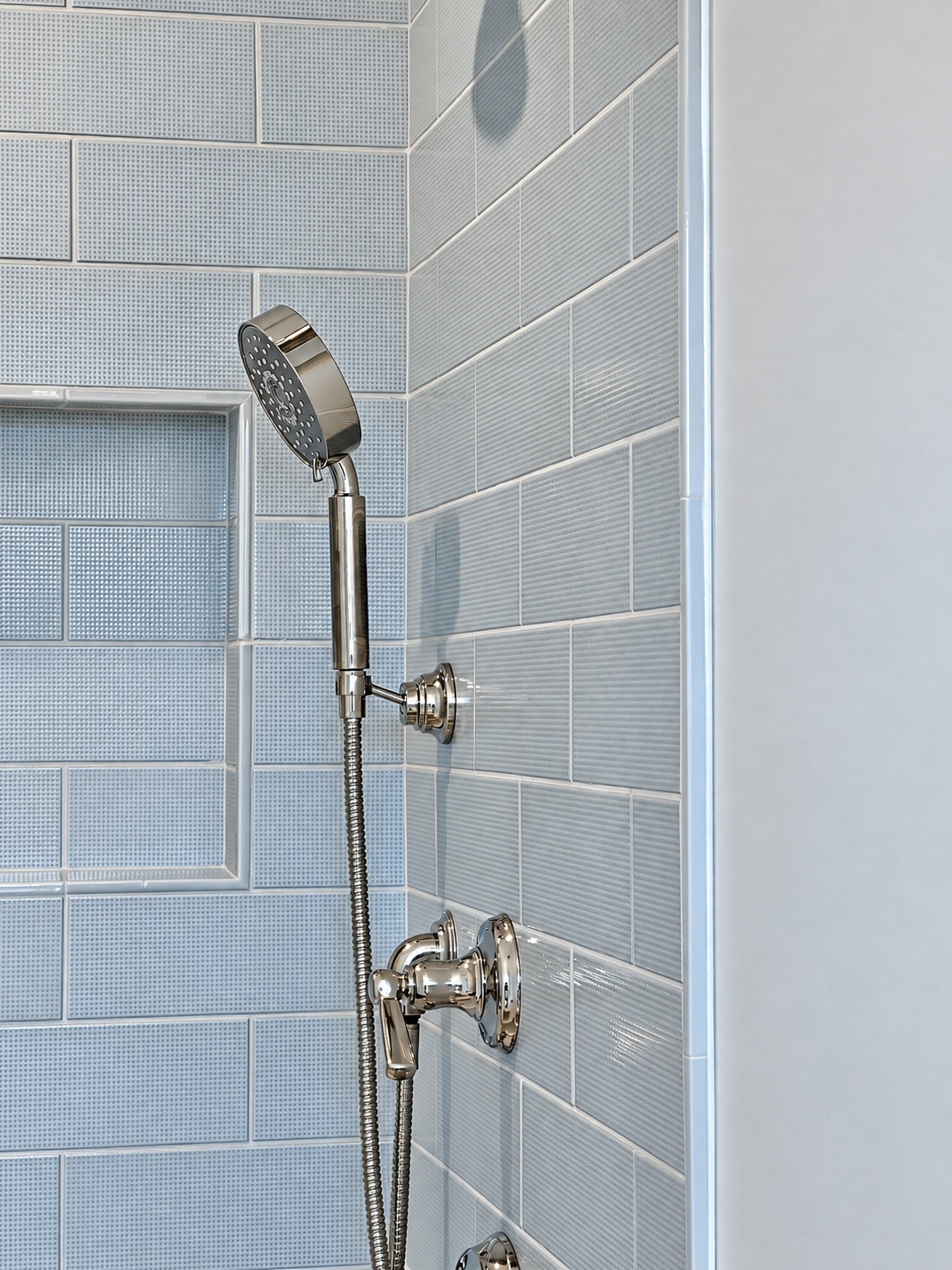 Textured shower tiles with a recessed niche, precise corner joints and chrome fixtures