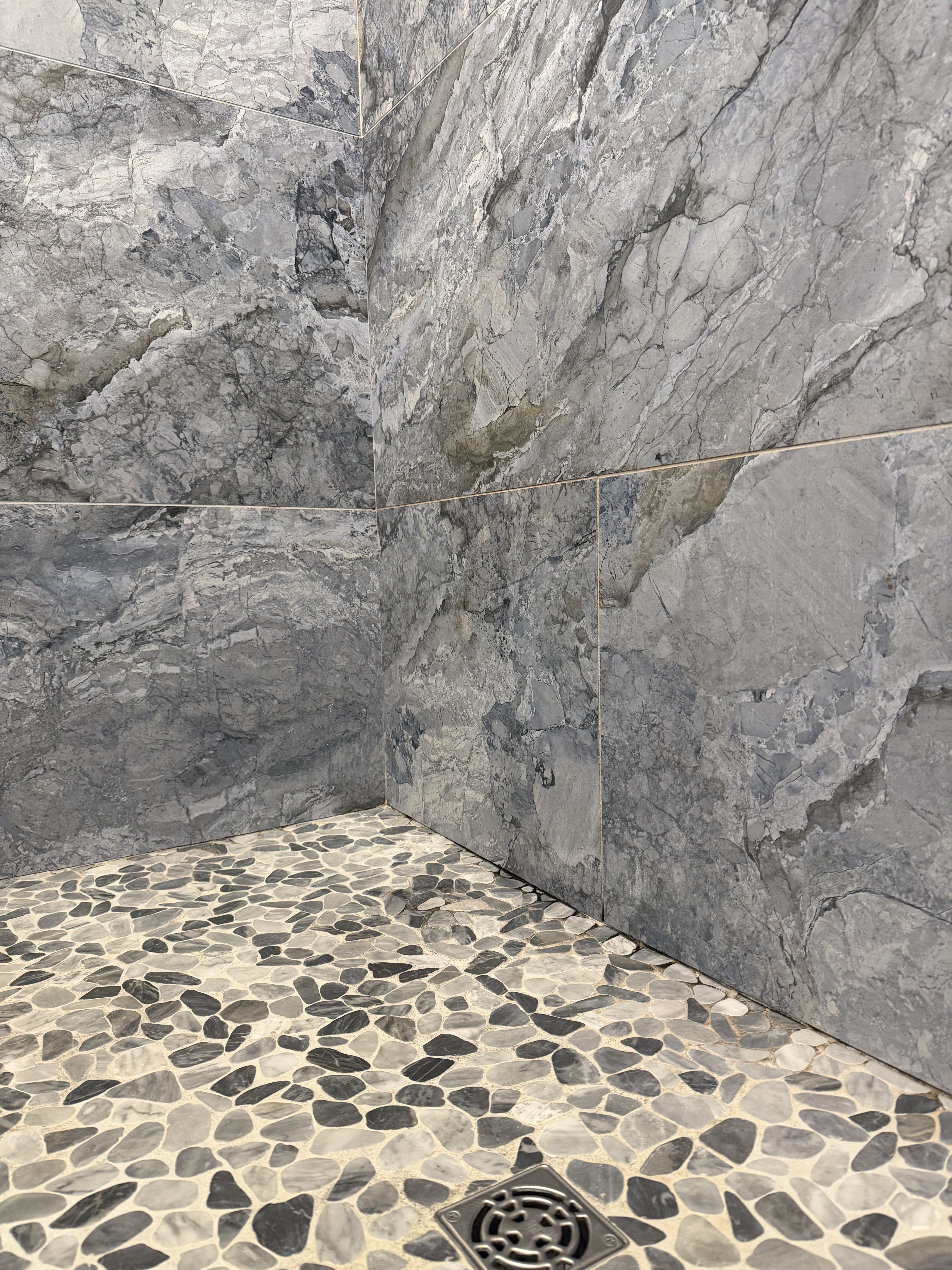 Marble shower corner meeting a pebble mosaic floor