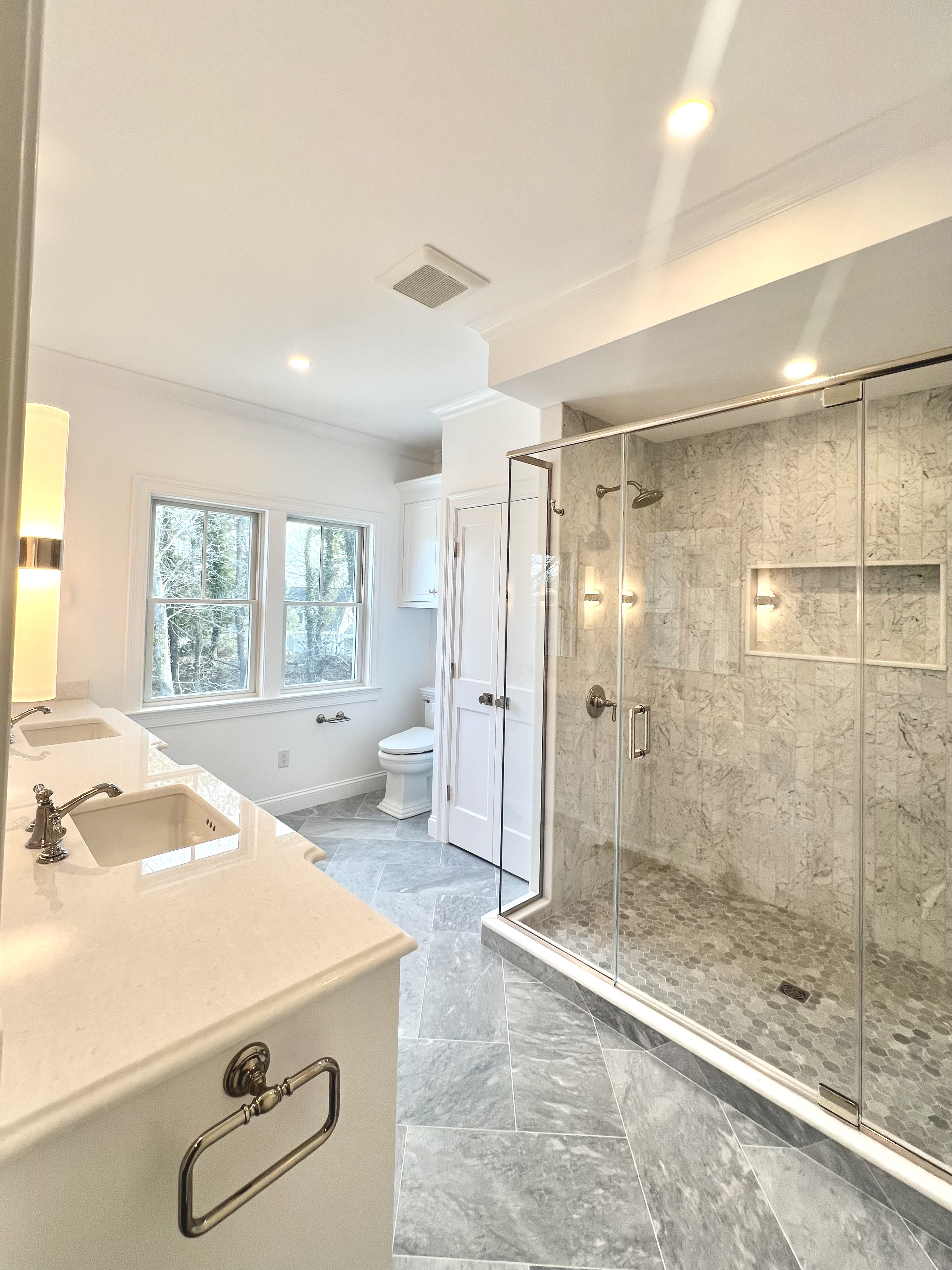 Remodeled bathroom with a glass-enclosed marble shower and double vanity