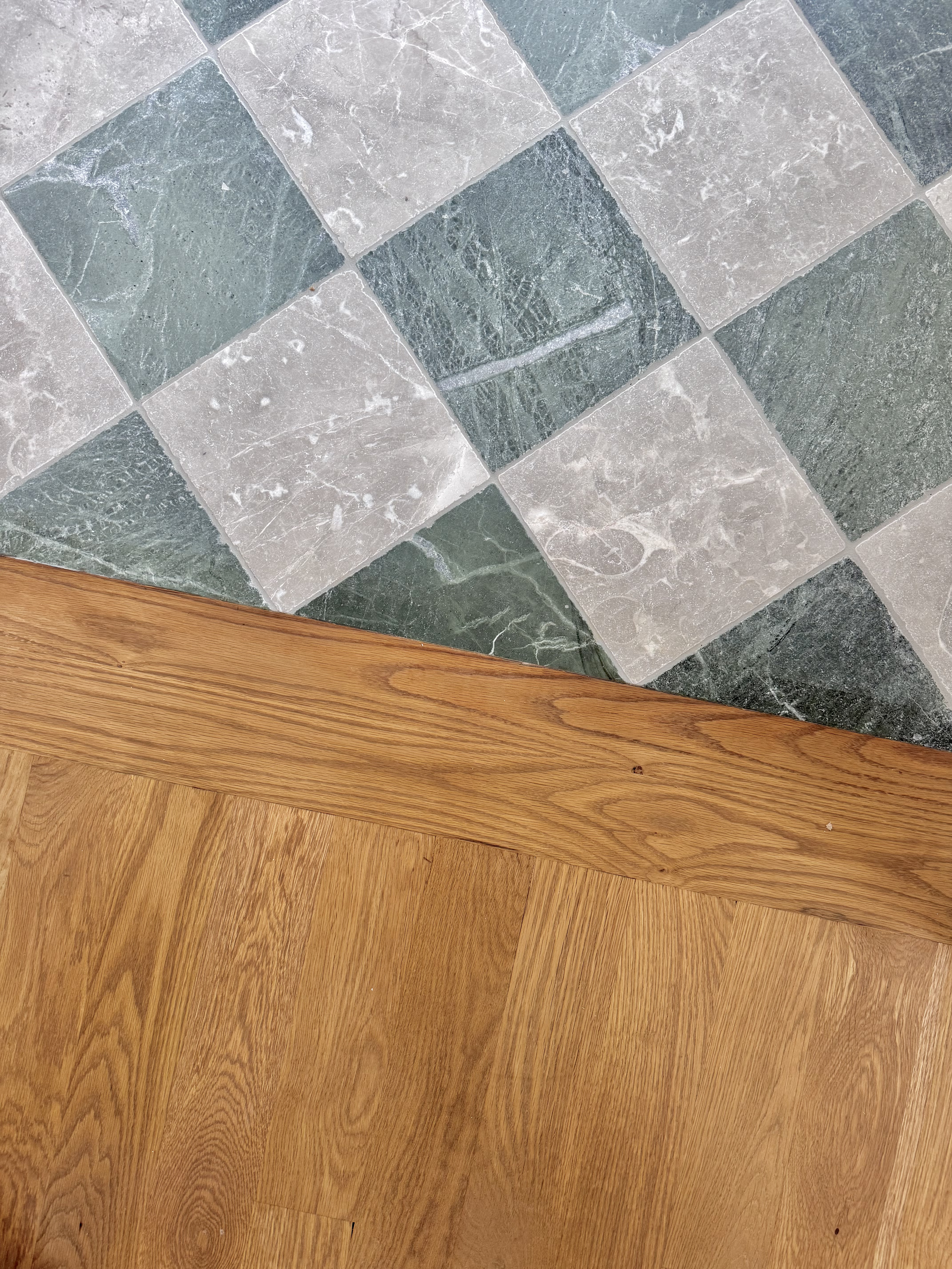 Diagonal checkerboard marble tile floor meeting a wood floor transition